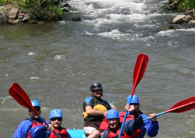 A group of four lifting their paddles in the air as they continue floating down the river.