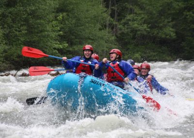 A group of six paddling down the Klickitat whitewater rafting river and smiling as they hit a rapid.