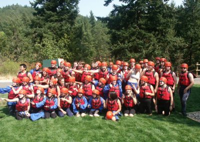 Huge group of young teens wearing rafting gear and pointing to one side.