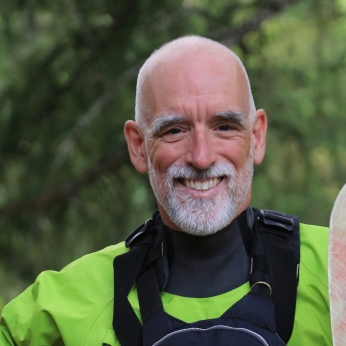 Older male guide and company owner, Mark, holding his raft paddle and smiling.